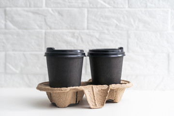 Takeaway paper coffee cups in cardboard holder on wooden table against black background, space for text.