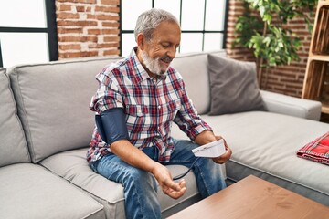 Fototapeta premium Senior grey-haired man measuring pulse using tensiometer at home