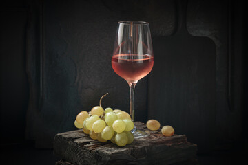 Glass of rose wine with ripe white grapes on dark background still life with copy space. Drinking...