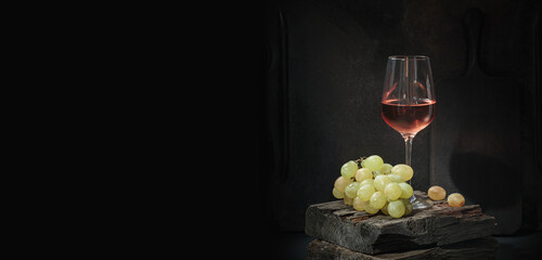 Glass of rose wine with ripe white grapes on dark background still life with copy space. Drinking wine concept