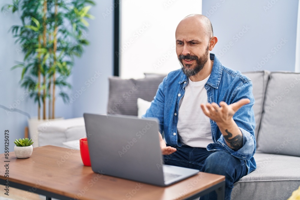 Sticker Young bald man having video call sitting on sofa at home