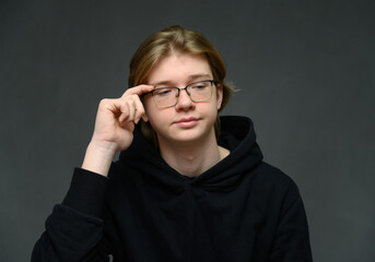 Caucasian guy portrait adjusts his glasses on a gray background looking at the camera