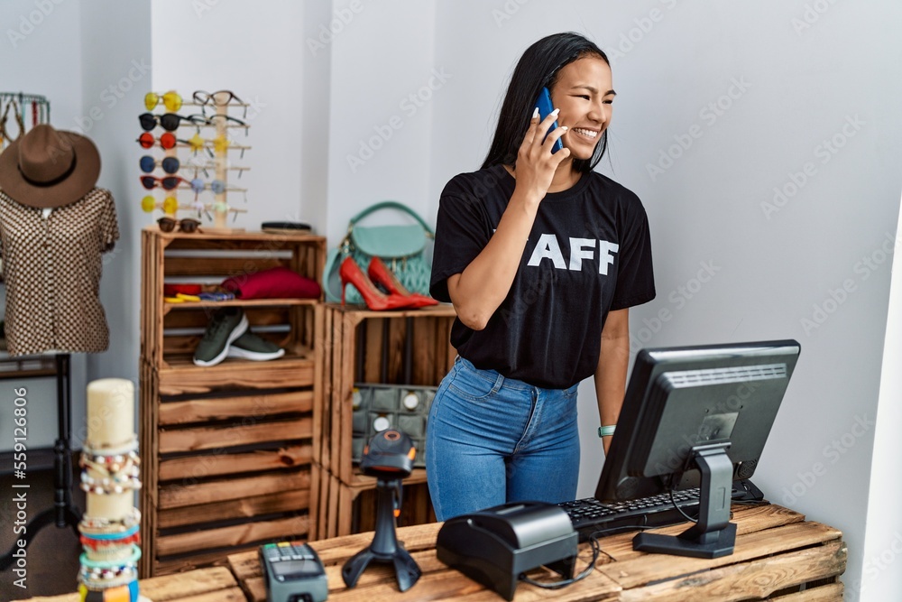 Poster Young latin woman talking on the smartphone working at clothing store