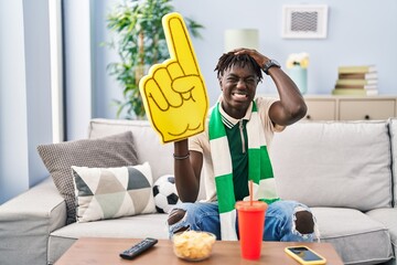 African man with dreadlocks football hooligan supporting team stressed and frustrated with hand on head, surprised and angry face