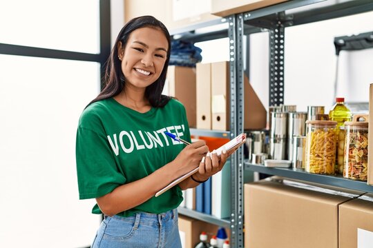 Young latin woman wearing volunteer uniform working at charity center