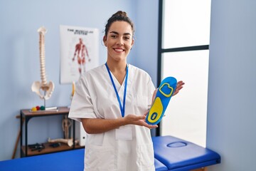 Young hispanic woman holding shoe insole at physiotherapy clinic smiling with a happy and cool smile on face. showing teeth.