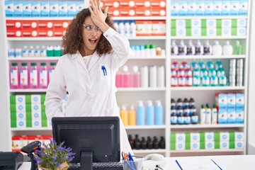Hispanic woman with curly hair working at pharmacy drugstore surprised with hand on head for...