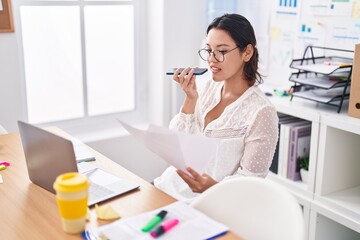 Young hispanic woman business worker talking on smartphone reading document at office