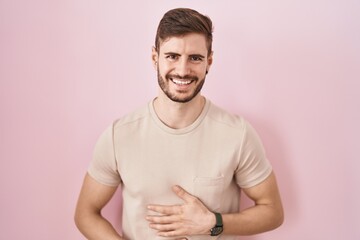 Hispanic man with beard standing over pink background smiling and laughing hard out loud because...