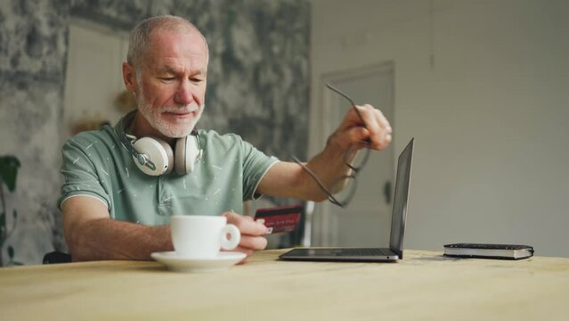Shopping from home. Old man enters card number for purchase in internet shop.