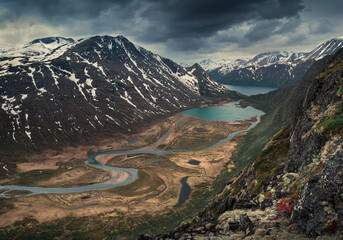 Turquoise lakes and river in mountain landscape from above the hike to Knutshoe summit in Jotunheimen National Park in Norway, snow-covered mountains of Besseggen in background - obrazy, fototapety, plakaty