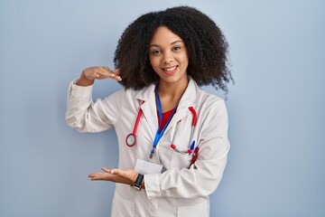 Young african american woman wearing doctor uniform and stethoscope gesturing with hands showing big and large size sign, measure symbol. smiling looking at the camera. measuring concept.
