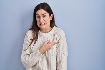 Young brunette woman standing over blue background pointing aside worried and nervous with...