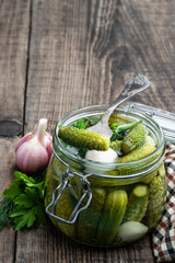 Pickled cucumbers in glass jar on wooden table