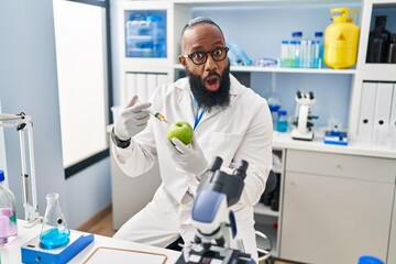 African american man working at scientist laboratory with apple afraid and shocked with surprise and amazed expression, fear and excited face.