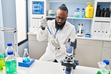 Young african american man wearing scientist uniform using pipette at laboratory