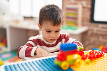 Adorable toddler playing with construction blocks sitting on table at kindergarten