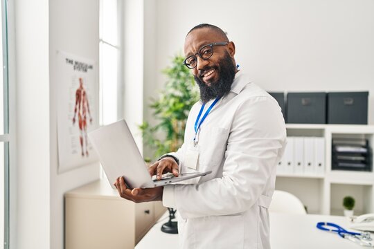 Young african american man wearing doctor uniform using laptop at clinic