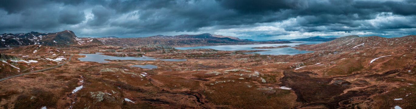 Panorama landscape with blue lakes, mountains and road of Jotunheimen National Park in Norway from above, dramatic dark cloudy sky