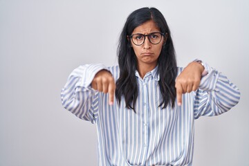 Young hispanic woman wearing glasses pointing down looking sad and upset, indicating direction with...