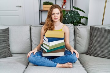 Young caucasian woman sitting on the sofa with books at home skeptic and nervous, frowning upset because of problem. negative person.