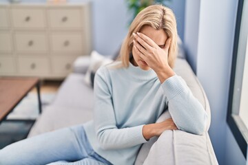 Young blonde woman stressed sitting on sofa at home