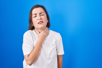 Middle age hispanic woman standing over blue background touching painful neck, sore throat for flu, clod and infection