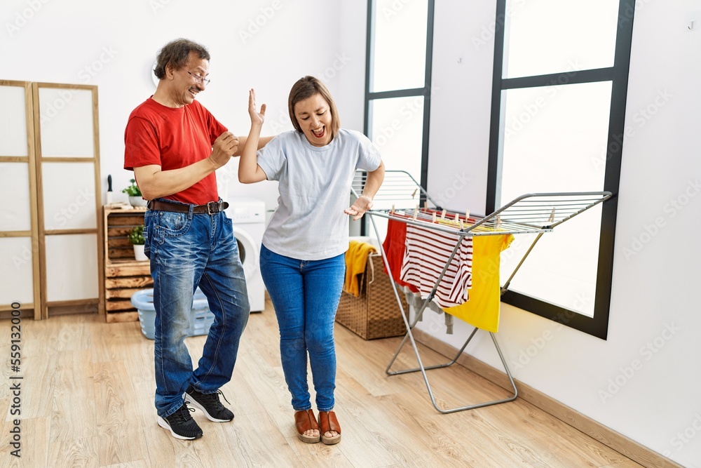 Wall mural middle age man and woman couple dancing waiting for washing machine at laundry