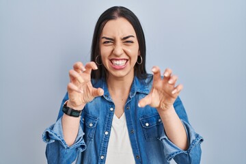 Hispanic woman standing over blue background smiling funny doing claw gesture as cat, aggressive and sexy expression