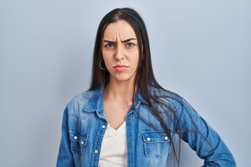 Hispanic woman standing over blue background skeptic and nervous, frowning upset because of...