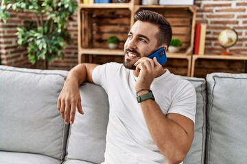 Young hispanic man smiling confident talking on the smartphone at home