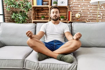 Fotobehang Lotusbloem Young hispanic man doing yoga exercise sitting on the sofa at home  © Krakenimages.com