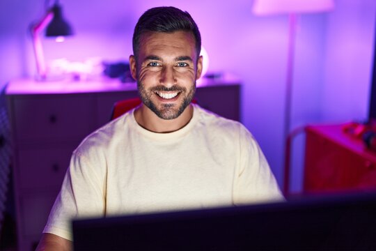 Young hispanic man streamer smiling confident sitting on table at gaming room
