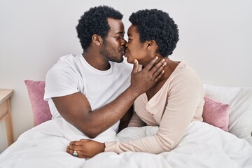 Fototapeta premium African american man and woman couple hugging each other and kissing sitting on bed at bedroom
