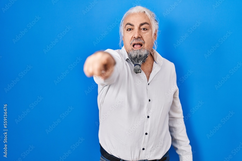 Poster Middle age man with grey hair standing over blue background pointing with finger surprised ahead, open mouth amazed expression, something on the front