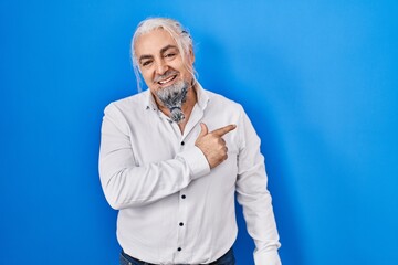 Middle age man with grey hair standing over blue background cheerful with a smile on face pointing with hand and finger up to the side with happy and natural expression
