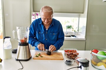 Senior man smiling confident cutting avocado at kitchen