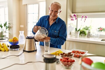 Senior man smiling confident pouring smoothie on glass at kitchen