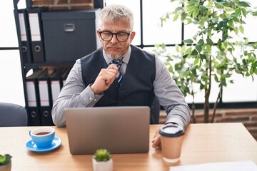 Middle age grey-haired man business worker using laptop with doubt expression at office