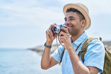 African american man tourist smiling confident using vintage camera at seaside