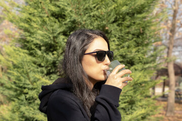 Holding glass, portrait of beautiful woman holding glass. Drinking still clean water. Sunny autumn day. Wearing sunglasses. Concept of health, walking outdoor, jogging, thirsty girl. Copy space.