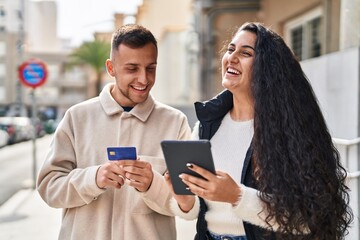 Man and woman smiling confident using touchpad and credit card at street