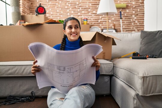 Young hispanic woman smiling confident looking house plans at new home