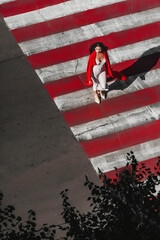 The dark-haired girl is dressed in extravagant evening clothes; a beautiful girl walks along the road through a pedestrian crossing; red lipstick on her lips