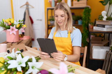 Young blonde woman florist smiling confident using touchpad at flower shop