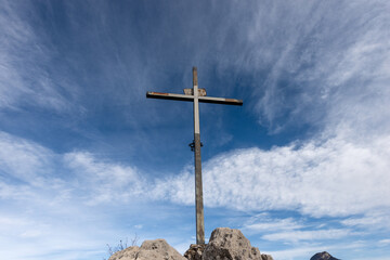 Metal religious cross on a mountain peak (Croce di Dos dela Cronela, Monte Altissimo di Nago, Sentiero della Pace) against a blue sky with clouds and copy space. Trentino Alto Adige, Italy, Europe.