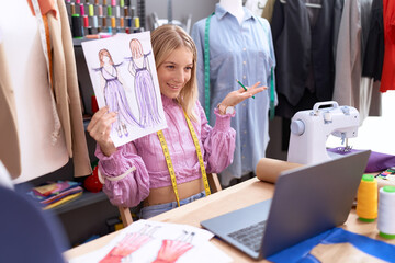 Young blonde woman tailor having video call showing clothing design at tailor shop