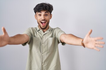 Arab man with beard standing over white background looking at the camera smiling with open arms for hug. cheerful expression embracing happiness.