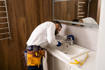 Professional plumber, male worker in uniform installing sink and water pipe in new apartment