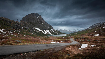 Mountain landscape of Litlefjellet Isfjorden with peak, road and lake in Norway Trollveggen, dramatic sky with dark clouds